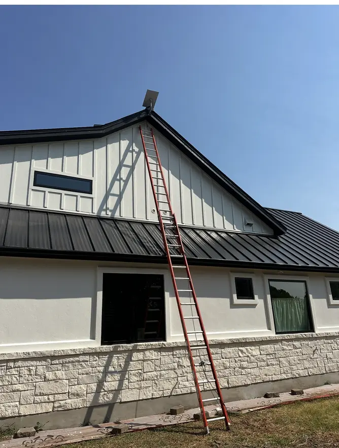 Ladder set against a metal-roof home for a Starlink install at the gable peak