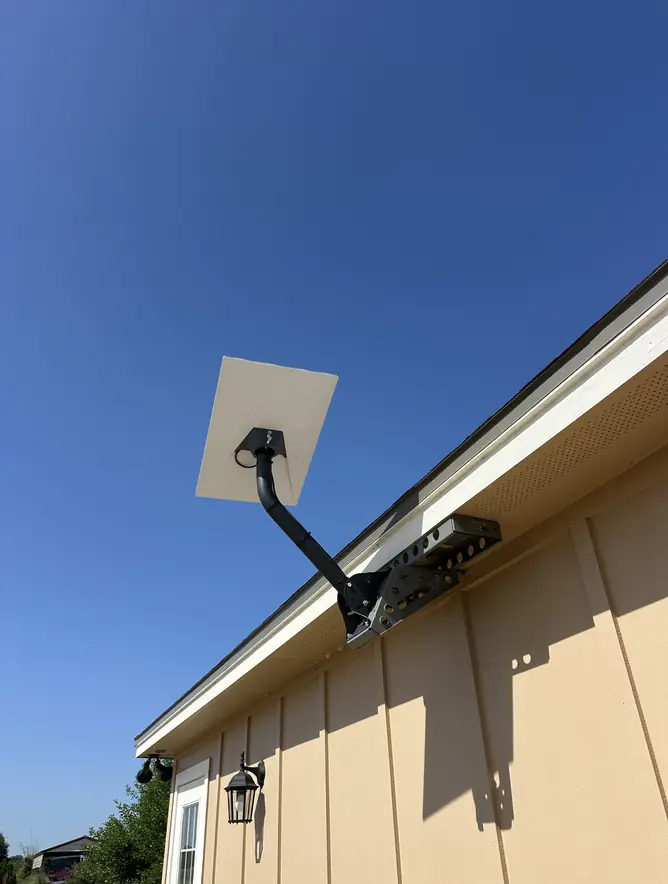 Starlink dish on a wall bracket at the roofline of a home with board-and-batten siding