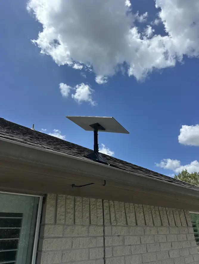 Starlink dish on a roof mount above a brick home, against a blue sky with clouds