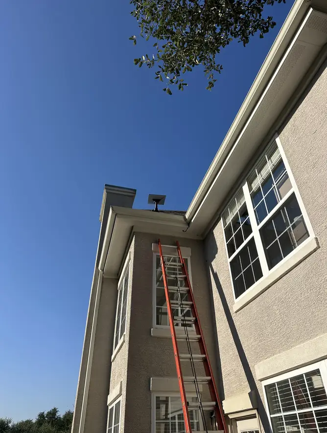 Ladder set up against a tall stucco home for a Starlink installation high on the roofline