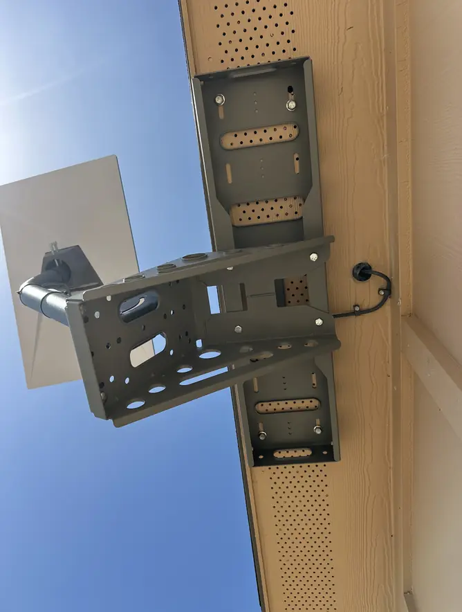 Heavy-duty Starlink wall bracket bolted under the eave, with the cable looped down to its entry point