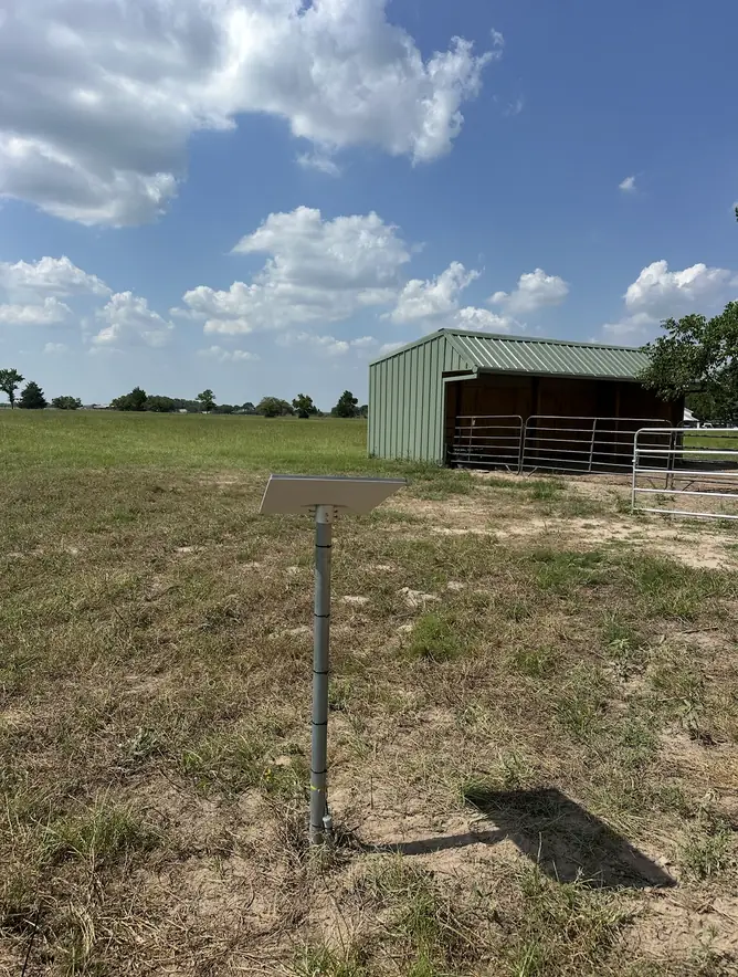 Starlink dish on a ground pole mount in a pasture near a metal barn