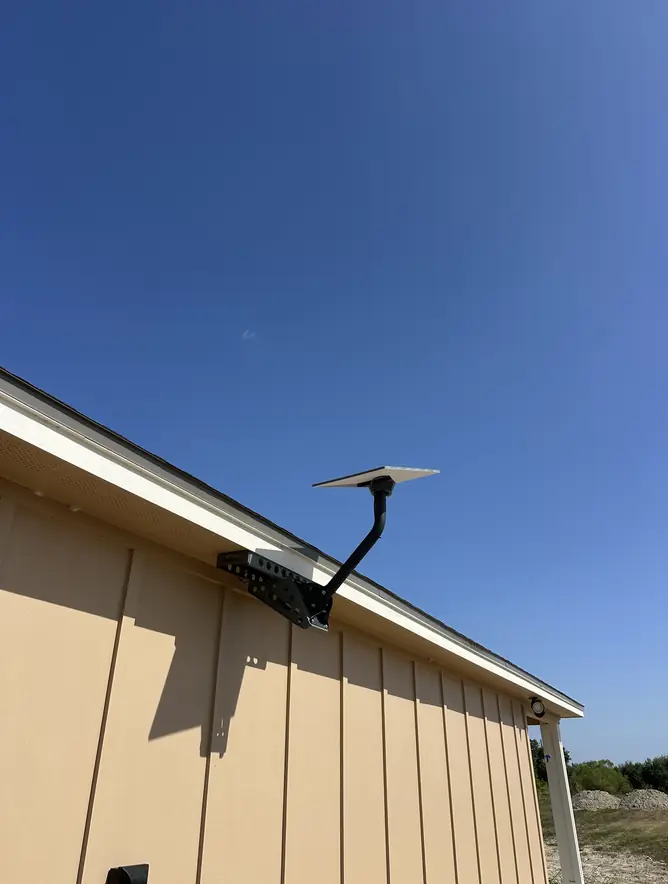 Starlink dish on a wall bracket at the gable end of a board-and-batten building