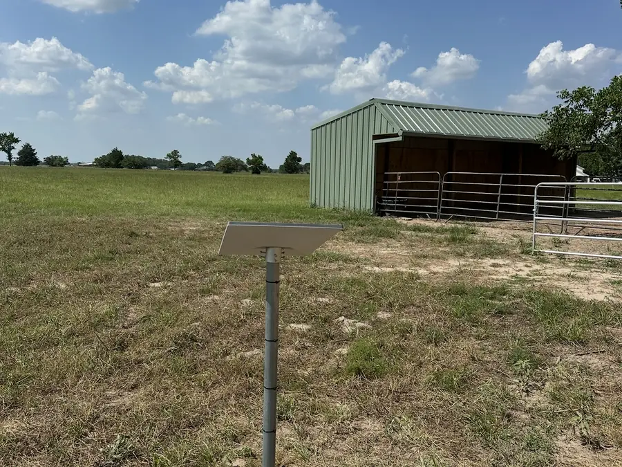 Starlink dish on a pole mount in a pasture beside a metal barn, ready to cover the outbuildings